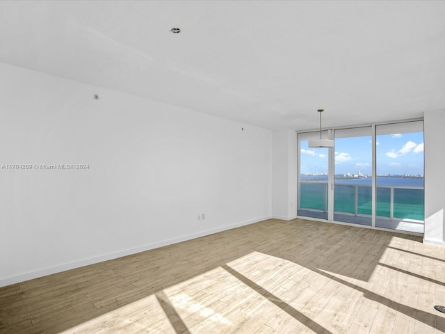 unfurnished room with floor to ceiling windows, light hardwood / wood-style flooring, and a water view