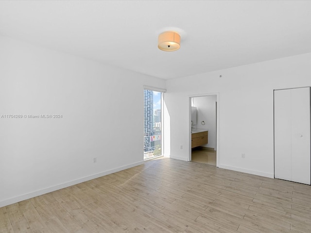 unfurnished bedroom featuring ensuite bathroom, a closet, and light wood-type flooring