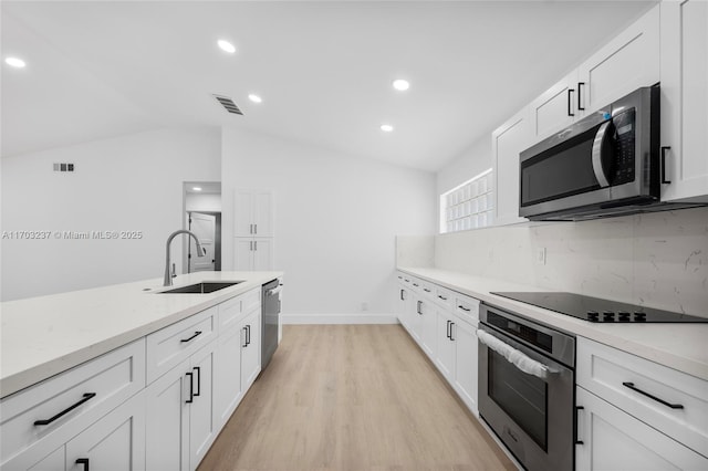 kitchen with vaulted ceiling, appliances with stainless steel finishes, sink, white cabinetry, and tasteful backsplash