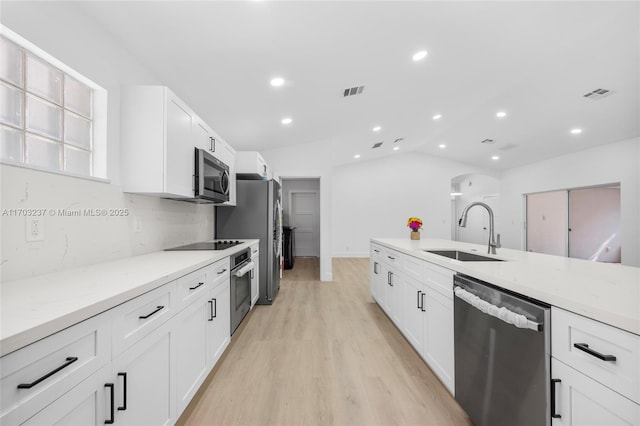 kitchen with light stone countertops, vaulted ceiling, white cabinets, appliances with stainless steel finishes, and sink