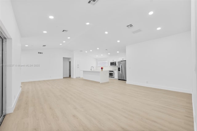 unfurnished living room with sink, light hardwood / wood-style flooring, and vaulted ceiling