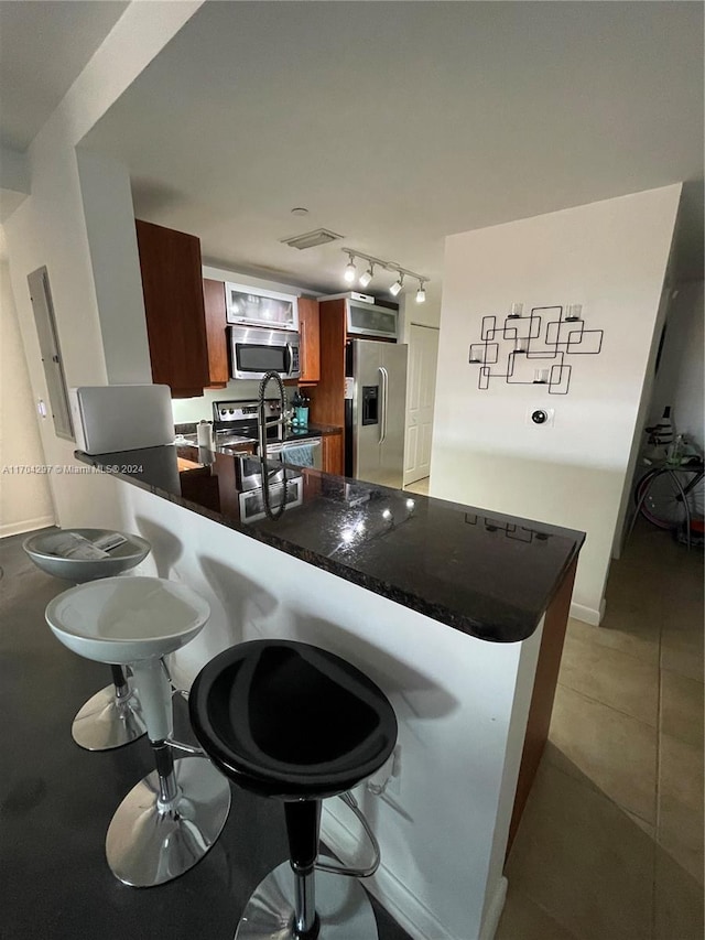 kitchen featuring kitchen peninsula, appliances with stainless steel finishes, a kitchen breakfast bar, and light tile patterned flooring