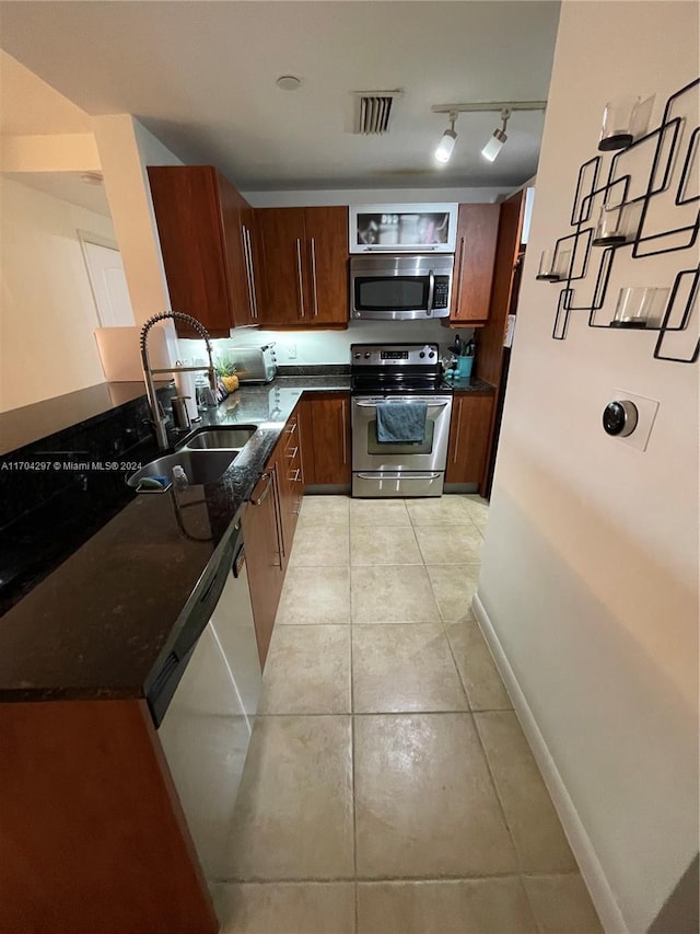 kitchen with light tile patterned flooring, dark stone countertops, sink, and appliances with stainless steel finishes