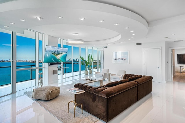 tiled living room with a wealth of natural light, a tray ceiling, and a wall of windows