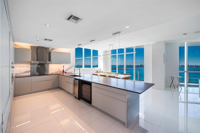 kitchen featuring kitchen peninsula, wall chimney exhaust hood, beverage cooler, sink, and decorative light fixtures