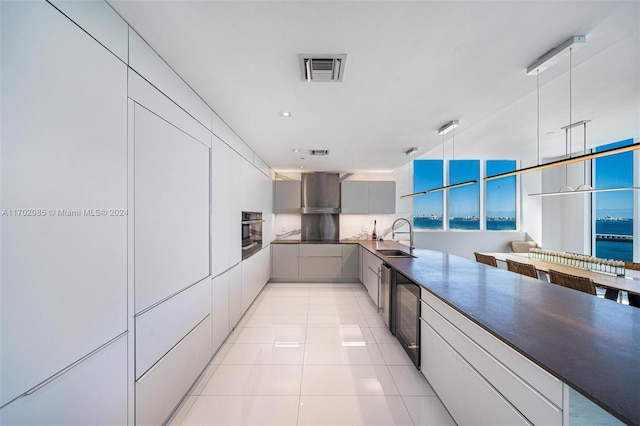 kitchen featuring sink, stainless steel oven, wall chimney range hood, pendant lighting, and gray cabinets