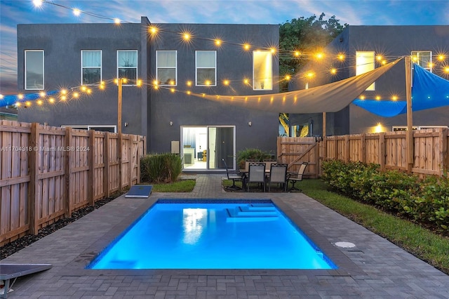 back house at dusk with a fenced in pool and a patio area