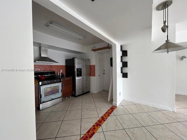 kitchen featuring stainless steel fridge, white gas stove, light tile patterned floors, and wall chimney range hood