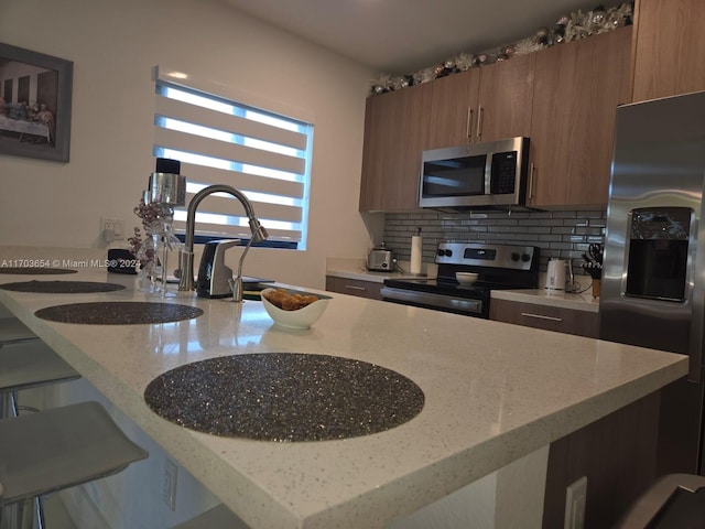 kitchen featuring backsplash, light stone countertops, a kitchen bar, and appliances with stainless steel finishes