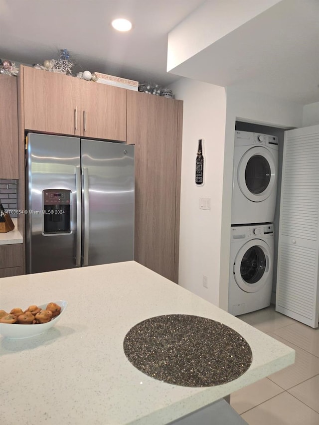 kitchen featuring stainless steel fridge, stacked washer and dryer, light tile patterned floors, and light stone countertops