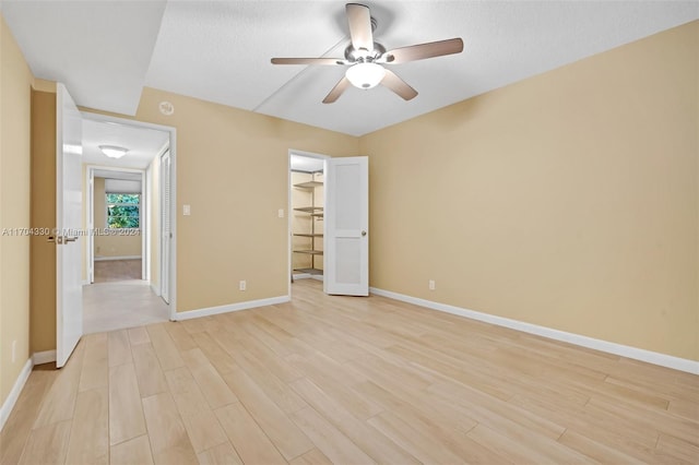 unfurnished bedroom with ceiling fan, light hardwood / wood-style floors, a textured ceiling, a walk in closet, and a closet