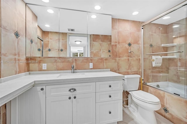 full bathroom with vanity, tile patterned floors, bath / shower combo with glass door, toilet, and tile walls