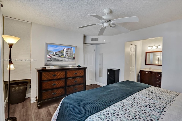 bedroom with a textured ceiling, ensuite bathroom, ceiling fan, and dark wood-type flooring