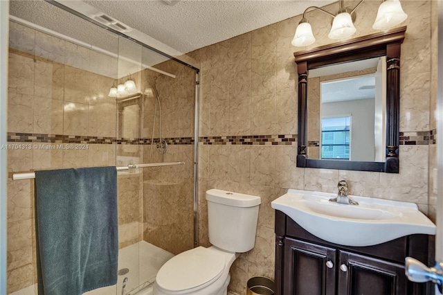 bathroom with a tile shower, a textured ceiling, toilet, vanity, and tile walls