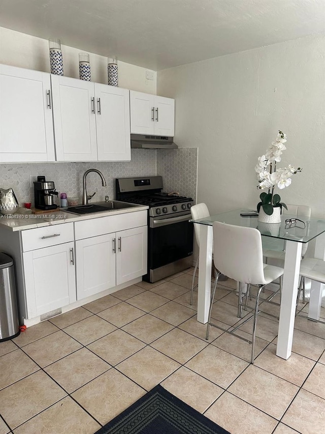 kitchen with backsplash, stainless steel range, sink, light tile patterned floors, and white cabinets