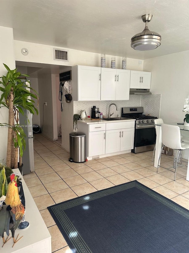 kitchen featuring sink, stainless steel gas stove, decorative backsplash, light tile patterned floors, and white cabinetry