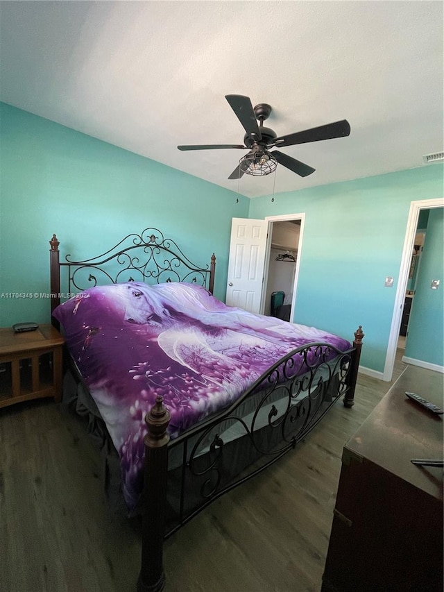 bedroom with a spacious closet, ceiling fan, wood-type flooring, and a closet