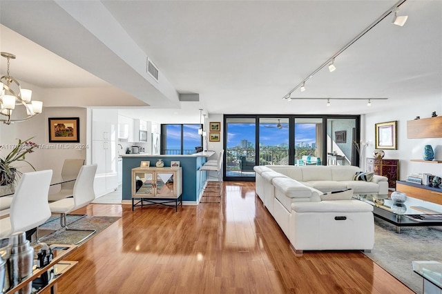 living room featuring expansive windows, light hardwood / wood-style floors, rail lighting, and an inviting chandelier