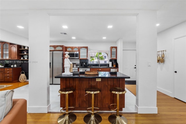 kitchen featuring a kitchen bar, tasteful backsplash, stainless steel appliances, sink, and light hardwood / wood-style flooring