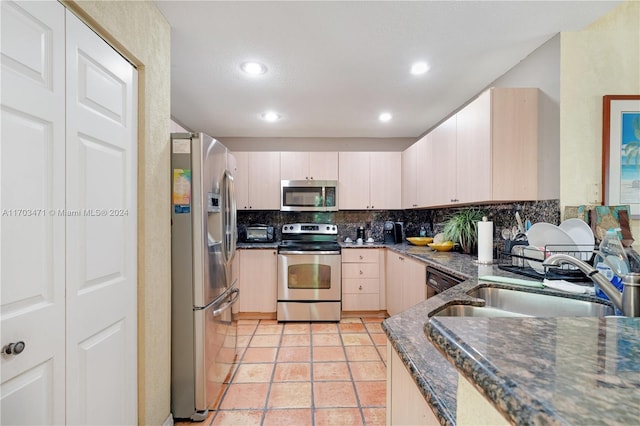 kitchen featuring dark stone counters, sink, decorative backsplash, light tile patterned floors, and appliances with stainless steel finishes