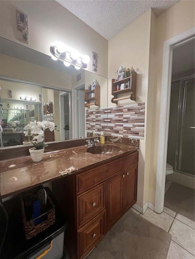 bathroom with backsplash, tile patterned flooring, toilet, a textured ceiling, and a shower with shower door