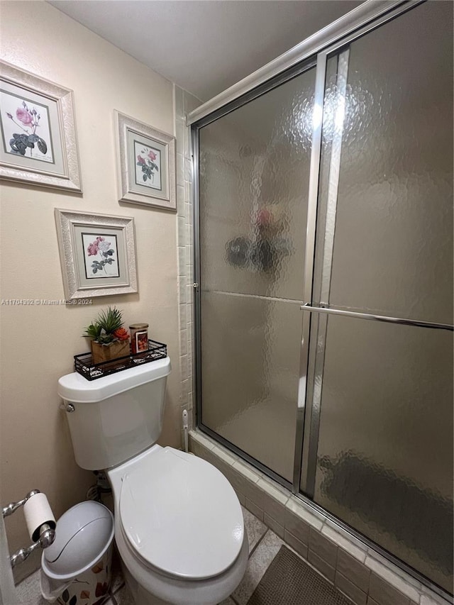 bathroom with tile patterned flooring, toilet, and a shower with shower door