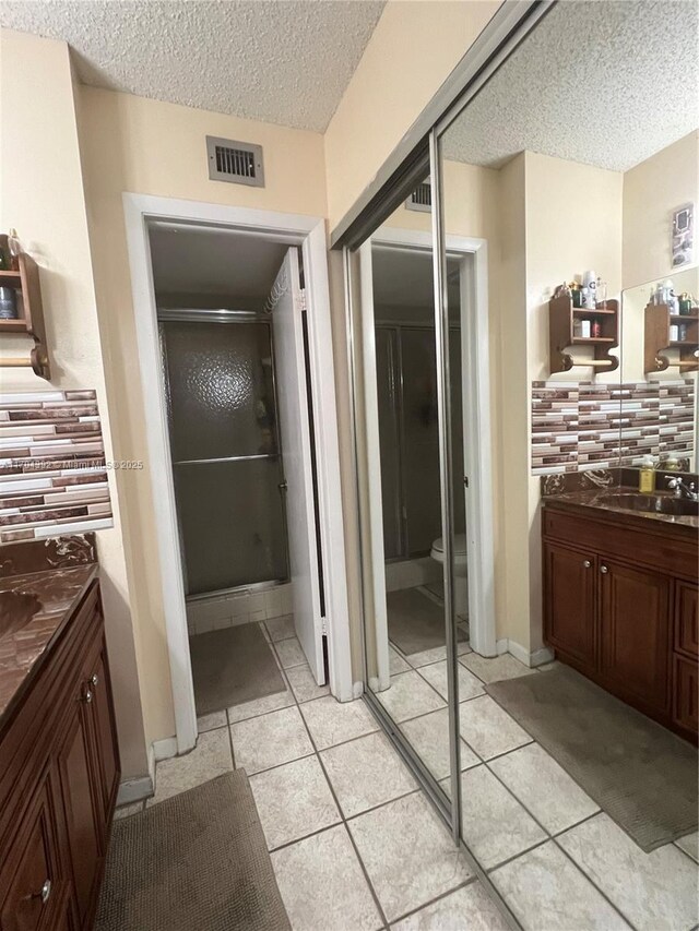 bathroom with tile patterned flooring, backsplash, a textured ceiling, a shower with door, and vanity