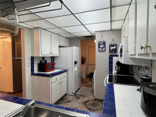 kitchen featuring white cabinetry, white refrigerator with ice dispenser, tile patterned floors, tile countertops, and backsplash