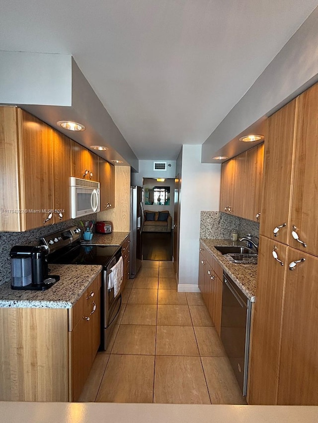 kitchen with tasteful backsplash, light stone counters, stainless steel appliances, sink, and light tile patterned floors