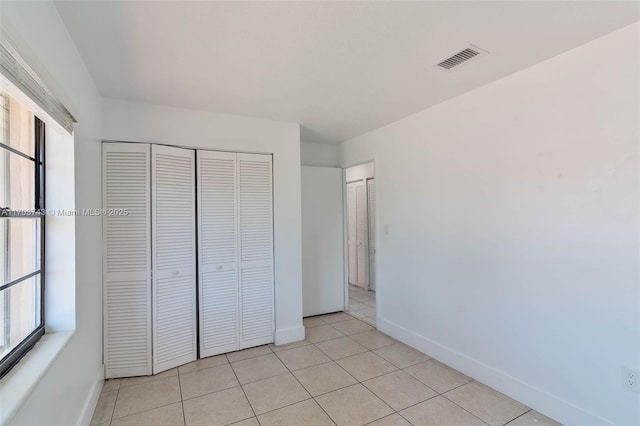 unfurnished bedroom with multiple windows, light tile patterned floors, and a closet