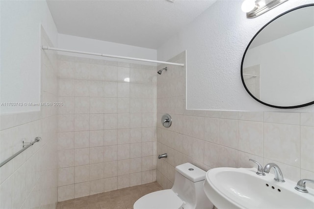 bathroom featuring tile walls, sink, toilet, and tiled shower