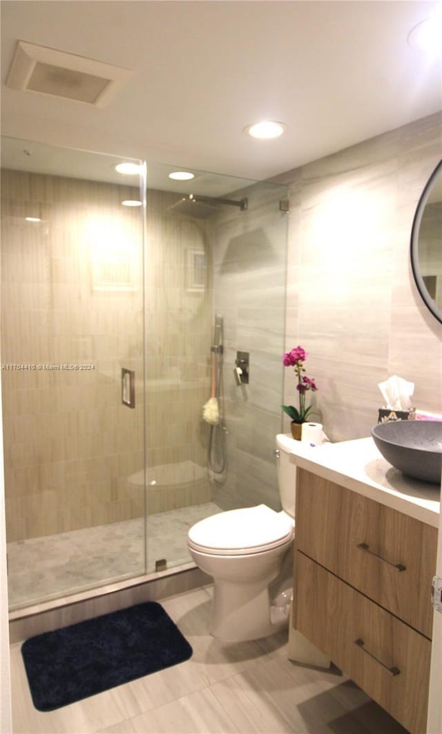 bathroom with vanity, toilet, an enclosed shower, and tile walls