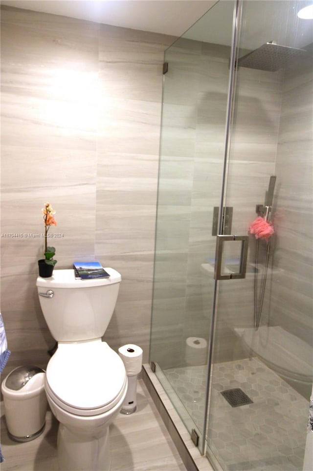 bathroom with tile patterned flooring, toilet, a shower with door, and tile walls