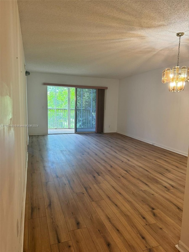 empty room featuring wood-type flooring, a textured ceiling, and a notable chandelier