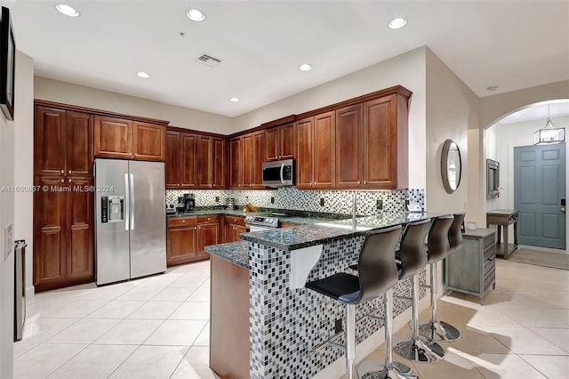 kitchen with backsplash, dark stone countertops, light tile patterned floors, kitchen peninsula, and stainless steel appliances