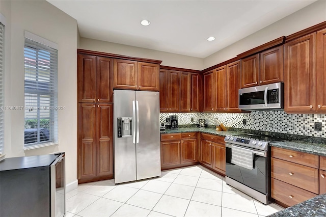 kitchen with light tile patterned flooring, dark stone countertops, appliances with stainless steel finishes, and tasteful backsplash