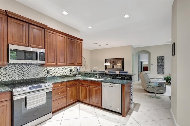 kitchen with tasteful backsplash, dark stone counters, stainless steel appliances, sink, and pendant lighting