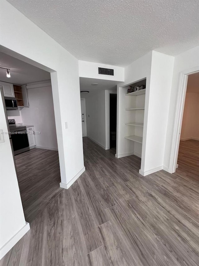 unfurnished living room with built in shelves, dark wood-type flooring, and a textured ceiling