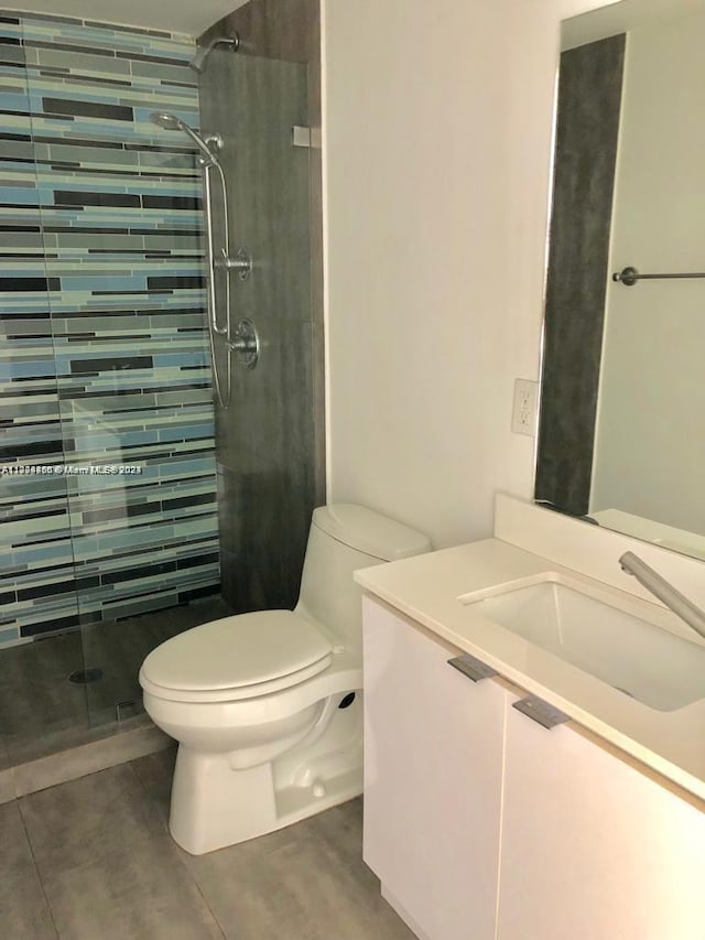 bathroom with tiled shower, tile patterned flooring, vanity, and toilet