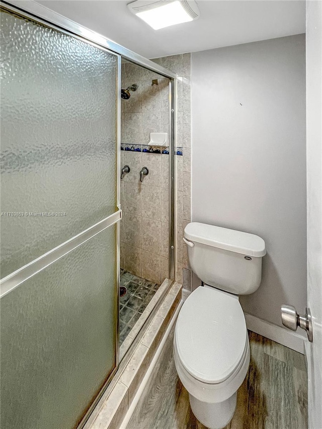 bathroom with hardwood / wood-style floors, toilet, and an enclosed shower