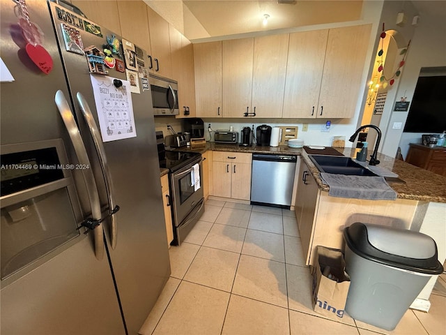 kitchen featuring light brown cabinets, dark stone counters, sink, light tile patterned floors, and appliances with stainless steel finishes