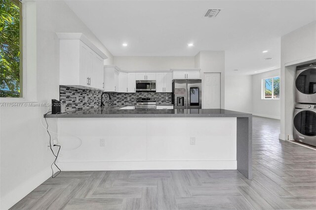 kitchen featuring kitchen peninsula, appliances with stainless steel finishes, white cabinets, and stacked washing maching and dryer