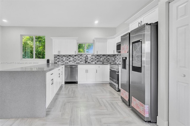 kitchen with appliances with stainless steel finishes, tasteful backsplash, sink, light parquet flooring, and white cabinetry