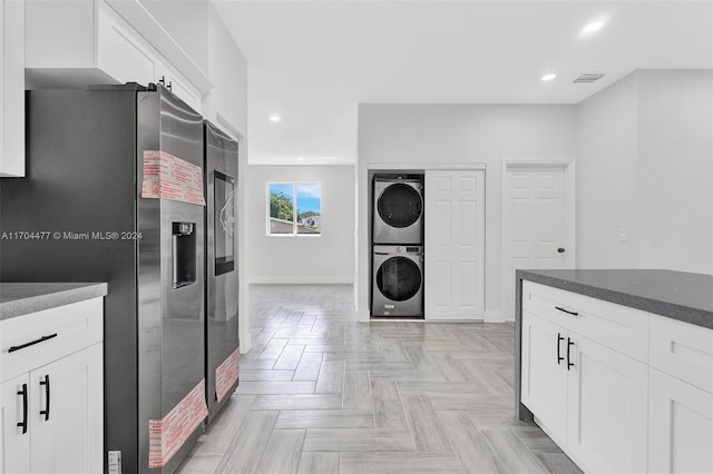 kitchen with stainless steel fridge, stacked washing maching and dryer, white cabinetry, and light parquet flooring