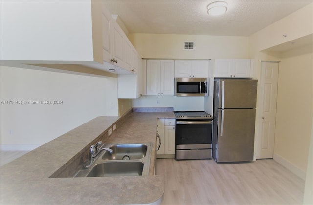 kitchen featuring white cabinetry, sink, stainless steel appliances, light hardwood / wood-style flooring, and a textured ceiling