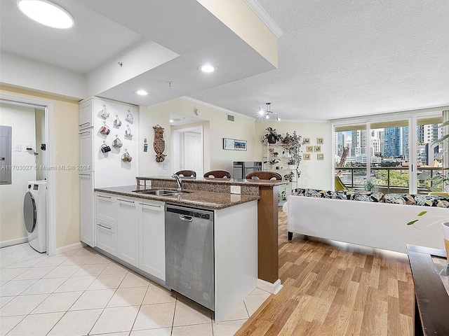 kitchen with dishwasher, sink, light wood-type flooring, washer / dryer, and white cabinetry