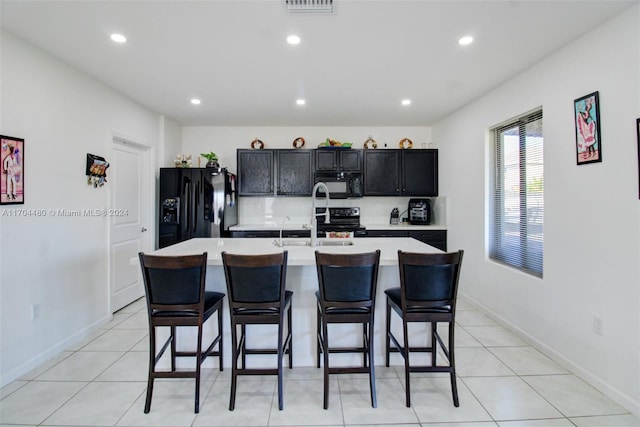 kitchen with black appliances, light tile patterned flooring, a center island with sink, and a kitchen bar