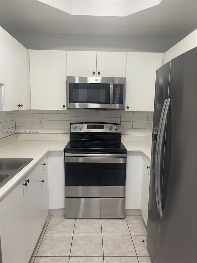 kitchen with white cabinets, appliances with stainless steel finishes, backsplash, and light tile patterned floors