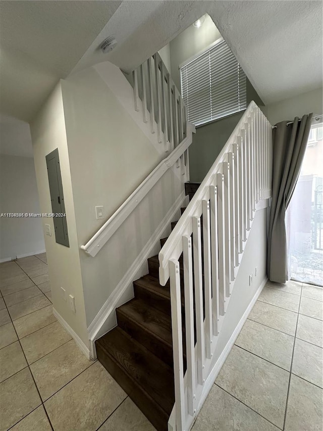 stairway with a textured ceiling, electric panel, and tile patterned floors