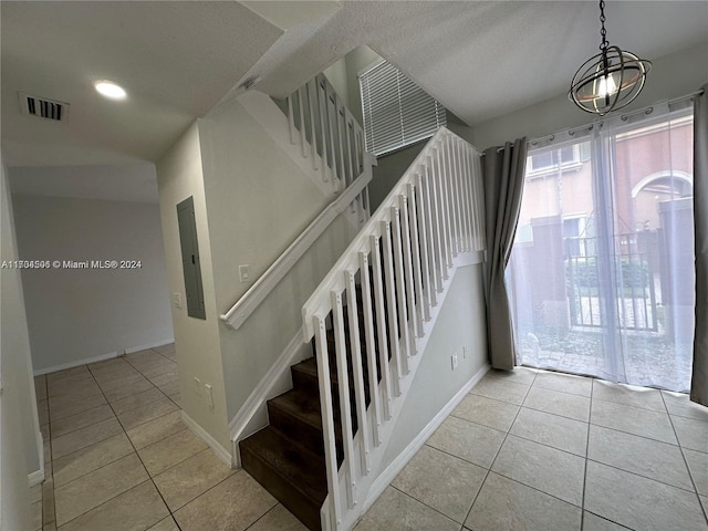 stairway with tile patterned flooring, electric panel, and a chandelier